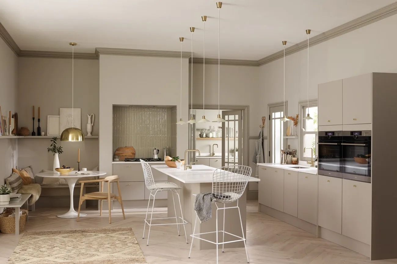 Modern open-plan kitchen with beige cabinetry, white island, gold accents, and a cozy dining nook with seating.