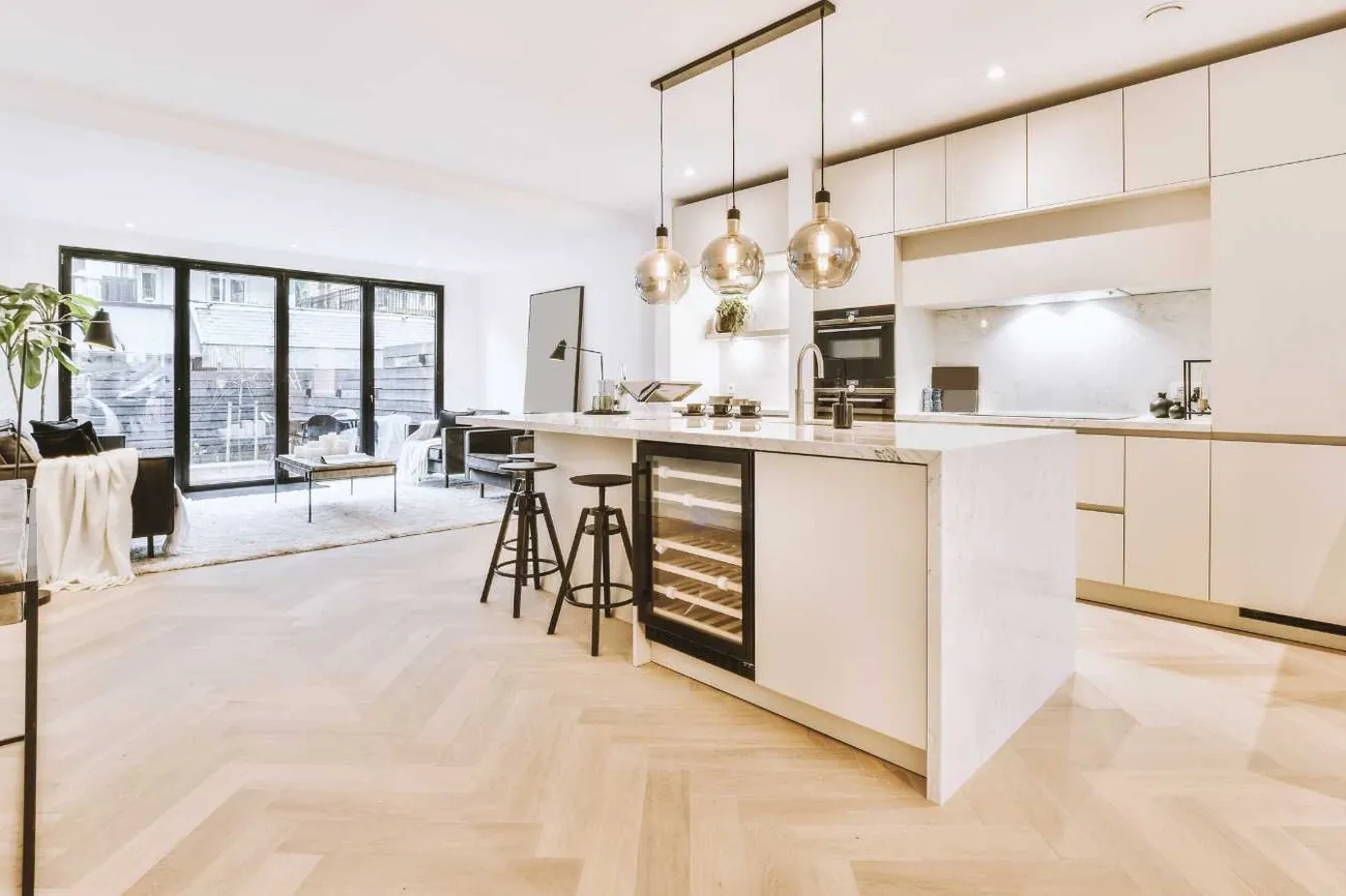 Modern open-concept kitchen and living room with marble island, pendant lights, and large glass doors leading outside.